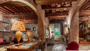 A rustic room with exposed brick walls, wooden beams, a stone fireplace, and a red chair. - PALAZZO PALESA B&B dimora storica (San Casciano dei Bagni)