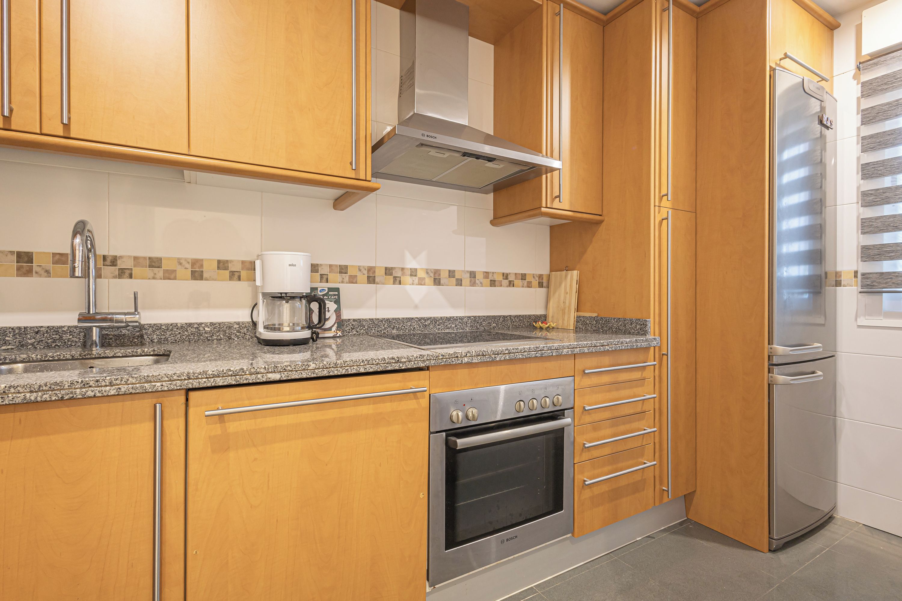 Eine Küche mit Holzausstattung, einem Edelstahlbackofen, einer Kaffeemaschine und einem Kühlschrank.