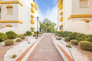 A pathway flanked by white buildings with yellow trim, leading to a palm tree-lined street. - Calanova Grand Golf (Mijas)