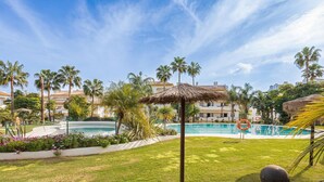 Zona de piscina amb palmeres, una sobrada de palla i un flotador.