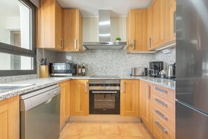 A kitchen with wooden cabinets, a stainless steel range hood, a built-in oven, a dishwasher, a refrigerator, and granite countertops. - Door To The Sun Estepona (Estepona)