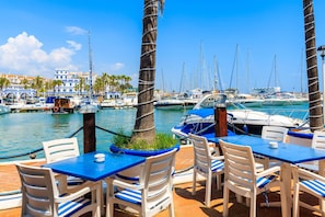 A marina with boats, palm trees, and a dining area with white chairs and blue tables. - Door To The Sun Estepona (Estepona)