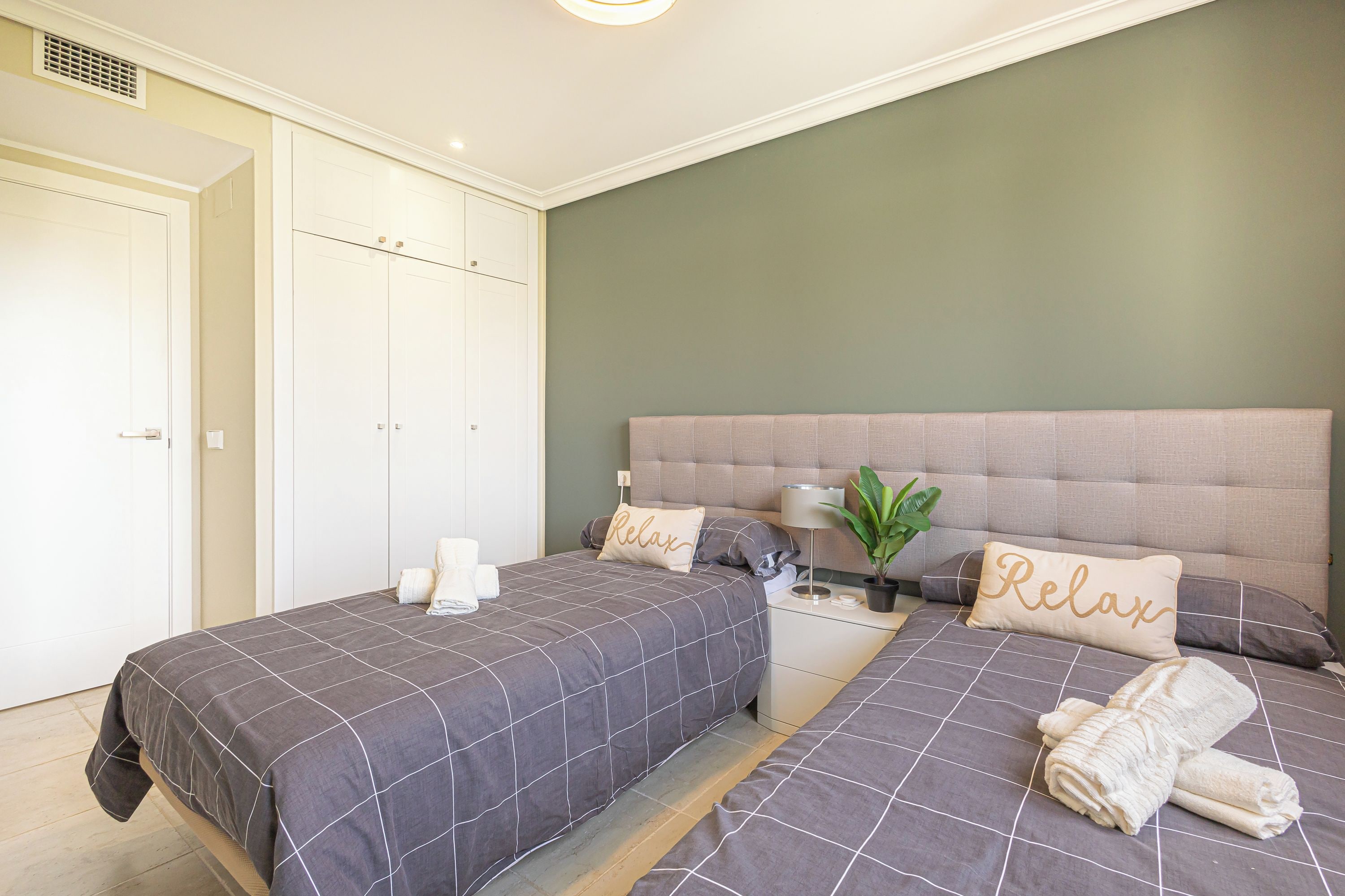 A bedroom with two beds, a bedside table, a nightstand, and a potted plant.