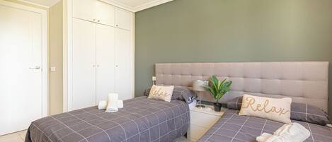 A bedroom with two beds, a bedside table, a nightstand, and a potted plant.