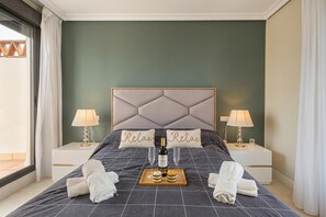 A neatly made bed with a headboard, two bedside tables with lamps, a tray with a bottle and glasses, and two pillows with the word 'Relax' on them. - Door To The Sun Estepona (Estepona)