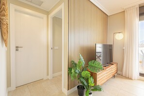 A modern hotel room with a wooden panel wall, a TV on a wooden console, a potted plant, and a view through a window. - Door To The Sun Estepona (Estepona)