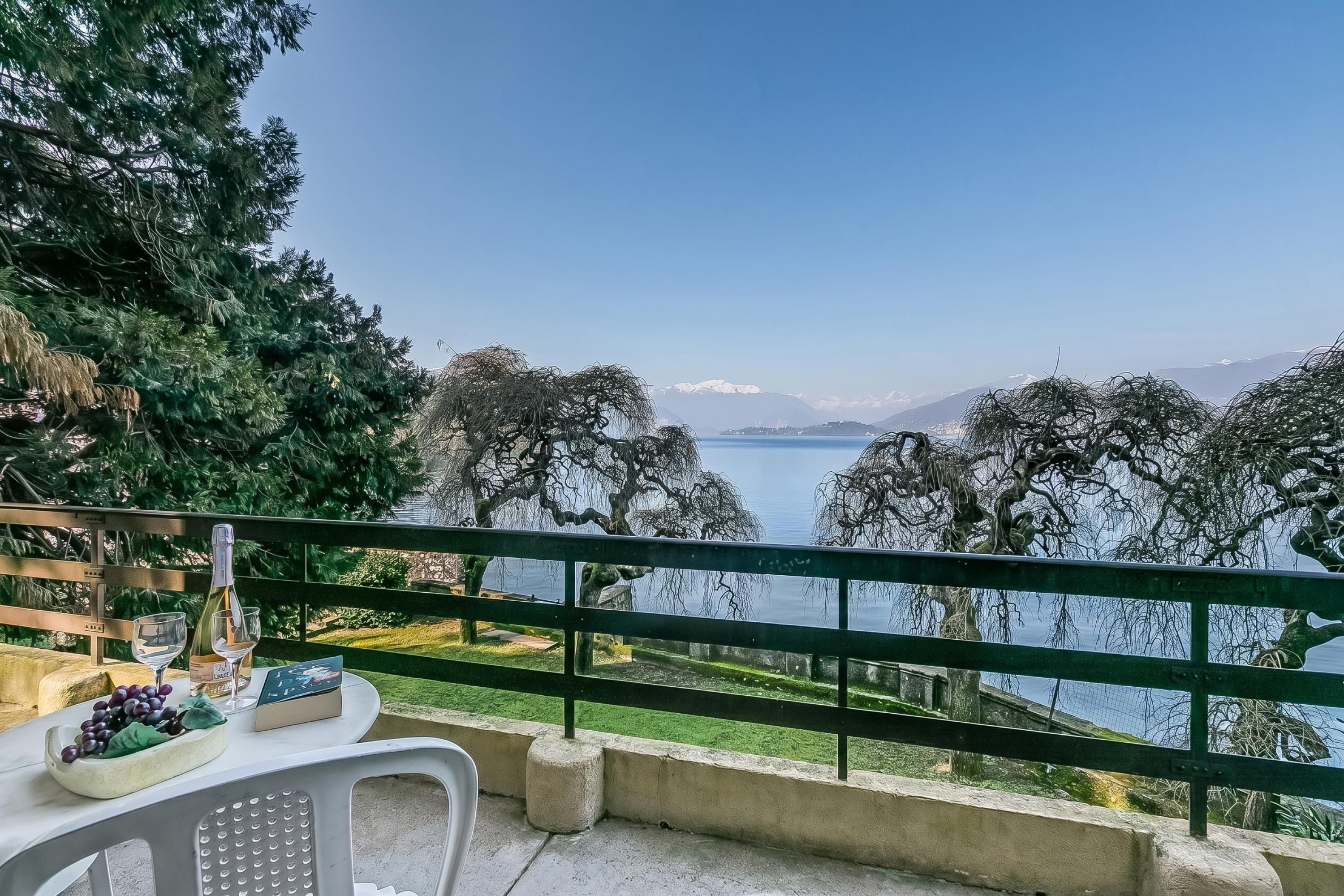 Terraço com mesa posta para refeições, com vista para um lago, árvores e montanhas ao fundo.