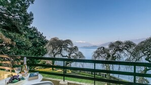 Una terraza con mesa lista para comer, con vistas a un lago, árboles y montañas al fondo.