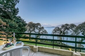 A terrace with a table set for dining, overlooking a lake with trees and mountains in the background. - Villa Incanto Sul Lago: Lakefront, Garden & Balconies (Laveno Mombello)