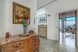 A room with a marble dresser, a vase with flowers, a framed painting, a telephone, and a view through a glass door. - Villa Incanto Sul Lago: Lakefront, Garden & Balconies (Laveno Mombello)
