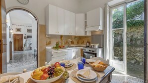 A kitchen with white cabinets, a dining table set with plates, glasses, and a bowl of fruit. - Villa Incanto Sul Lago: Lakefront, Garden & Balconies (Laveno Mombello)