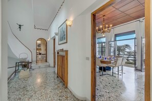 A spacious hallway with a tiled floor, a staircase, a dining area with a table and chairs, and a large window with a view. - Villa Incanto Sul Lago: Lakefront, Garden & Balconies (Laveno Mombello)