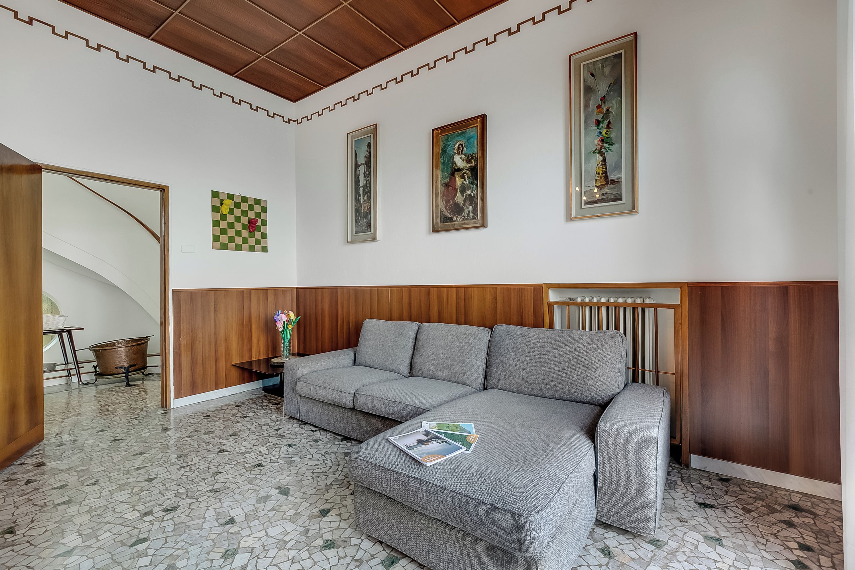Uma sala de estar moderna com um sofá seccional cinza, uma parede de destaque em madeira, piso ladrilhado e obras de arte emolduradas nas paredes.