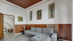 Una sala de estar moderna con un sofá seccional gris, un revestimiento de pared de madera, piso de baldosas y obras de arte enmarcadas en las paredes.