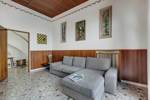 A modern living room with a grey sectional sofa, a wooden accent wall, a tiled floor, and framed artwork on the walls. - Villa Incanto Sul Lago: Lakefront, Garden & Balconies (Laveno Mombello)