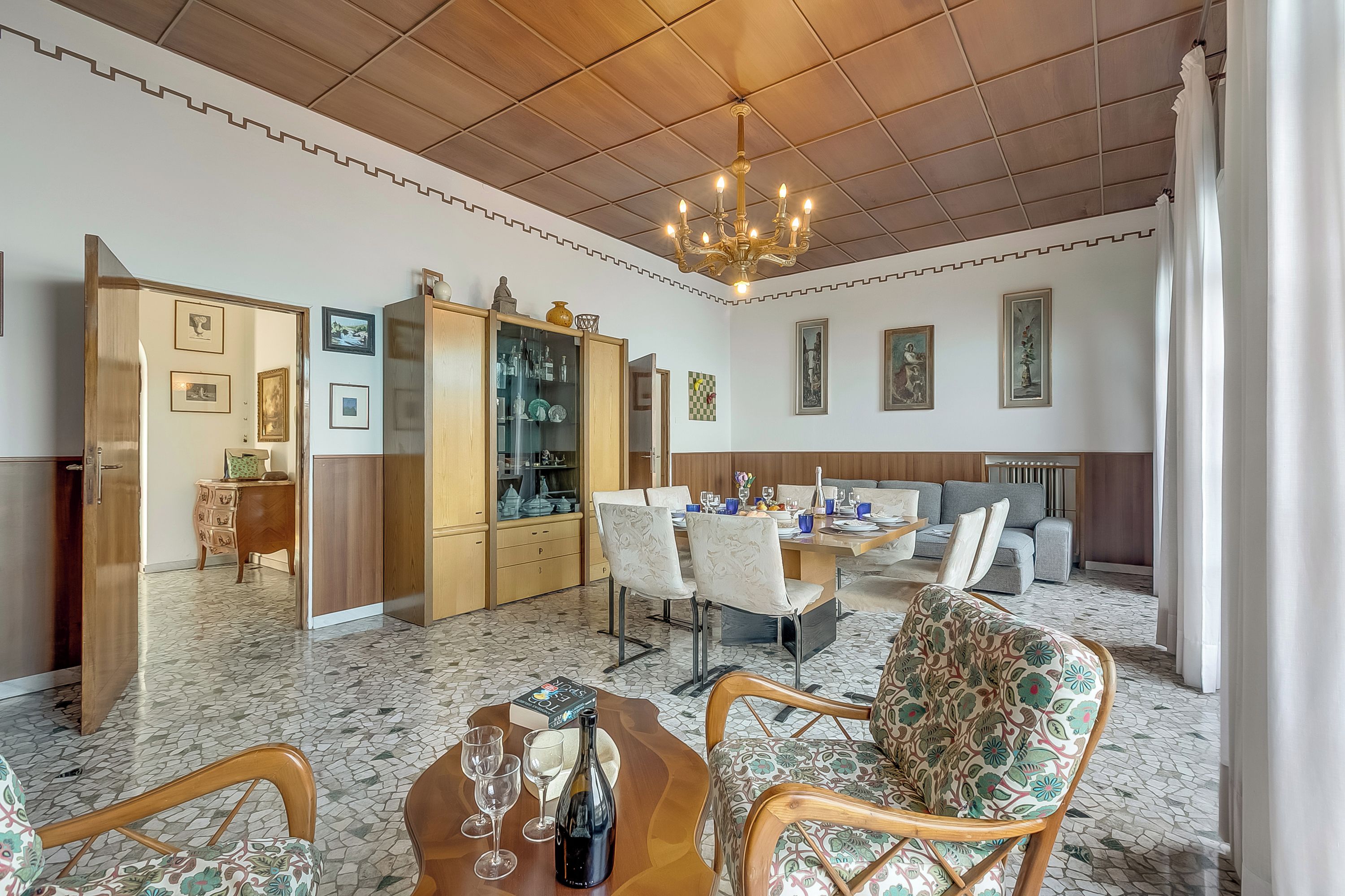 Uma sala de estar ampla com uma mesa de jantar, cadeiras, um sofá e um lustre.