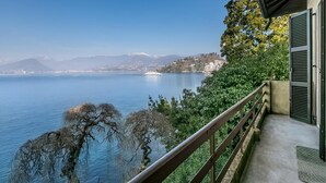 A balcony with a view of a lake, mountains, and a cruise ship. - Villa Incanto Sul Lago: Lakefront, Garden & Balconies (Laveno Mombello)