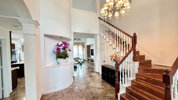 Un hallo espacioso con piso de mármol, una escalera de madera y un candelabro.