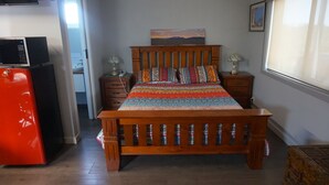 Una camera da letto con un letto di legno, un frigorifero rosso, un comodino in legno con una lampada e una finestra che si affaccia sul cielo.