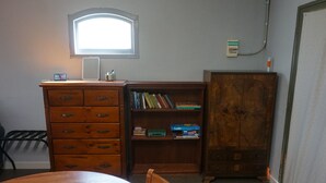 Una stanza con un comò in legno, una libreria, un tavolo con una ciotola verde e una finestra che lascia entrare luce naturale.