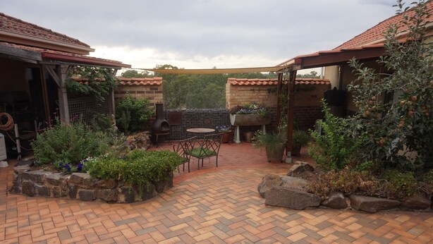 Una zona patio con pavimento in mattoni, un tavolo con sedie, un barbecue e piante in vaso.