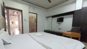 A hotel room with a bed, a wooden side table, a mirror, and a television mounted on the wall. - New Holiday Inn Hotel (Ajmer)