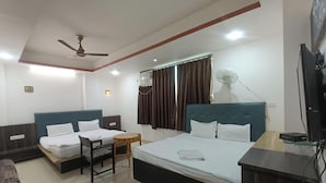 A hotel room with two beds, a ceiling fan, a TV, and a small table. - New Holiday Inn Hotel (Ajmer)