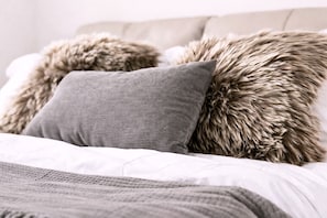 Un lit avec un drap blanc, un oreiller gris et un autre oreiller moelleux à la texture particulière.