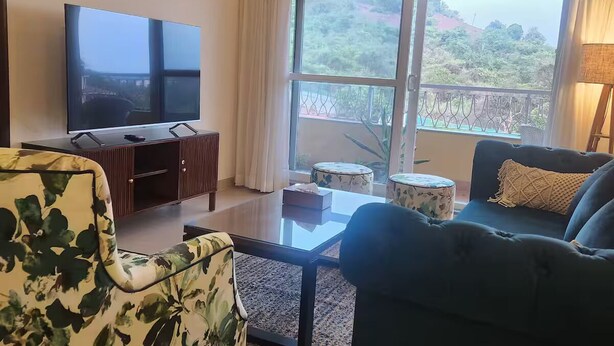 Ein Wohnzimmer mit Fernseher, Sofa, Couchtisch und Blick auf einen Balkon mit Pflanzen.