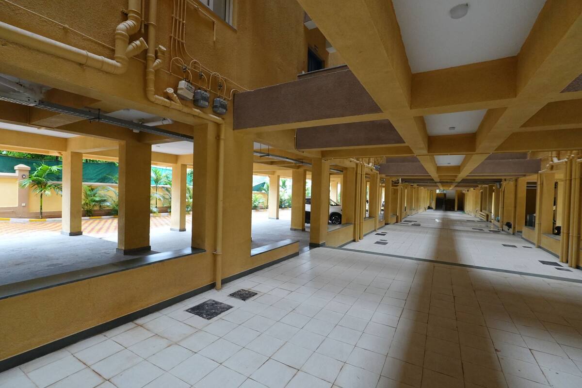 A long corridor with yellow walls and white tiled floors, leading to a covered outdoor area with greenery.