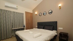Ein ordentlich bezogenes Bett mit weißen Leinentüchern und zwei aufgerollten Handtüchern, ein Nachttisch mit einer Lampe und eine Wand-Klimaanlage.
