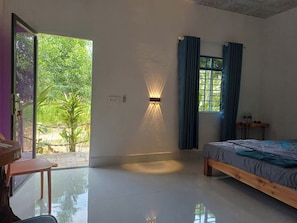 Ein Schlafzimmer mit Bett, Schreibtisch, Stuhl, einem Fenster mit Vorhängen und Blick ins Grüne.