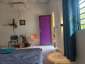 A room with a bed, two chairs, a small table, a purple door, and a window with curtains. - Lucky Home - Boutique Tropical Hideaway (Phu Quoc)