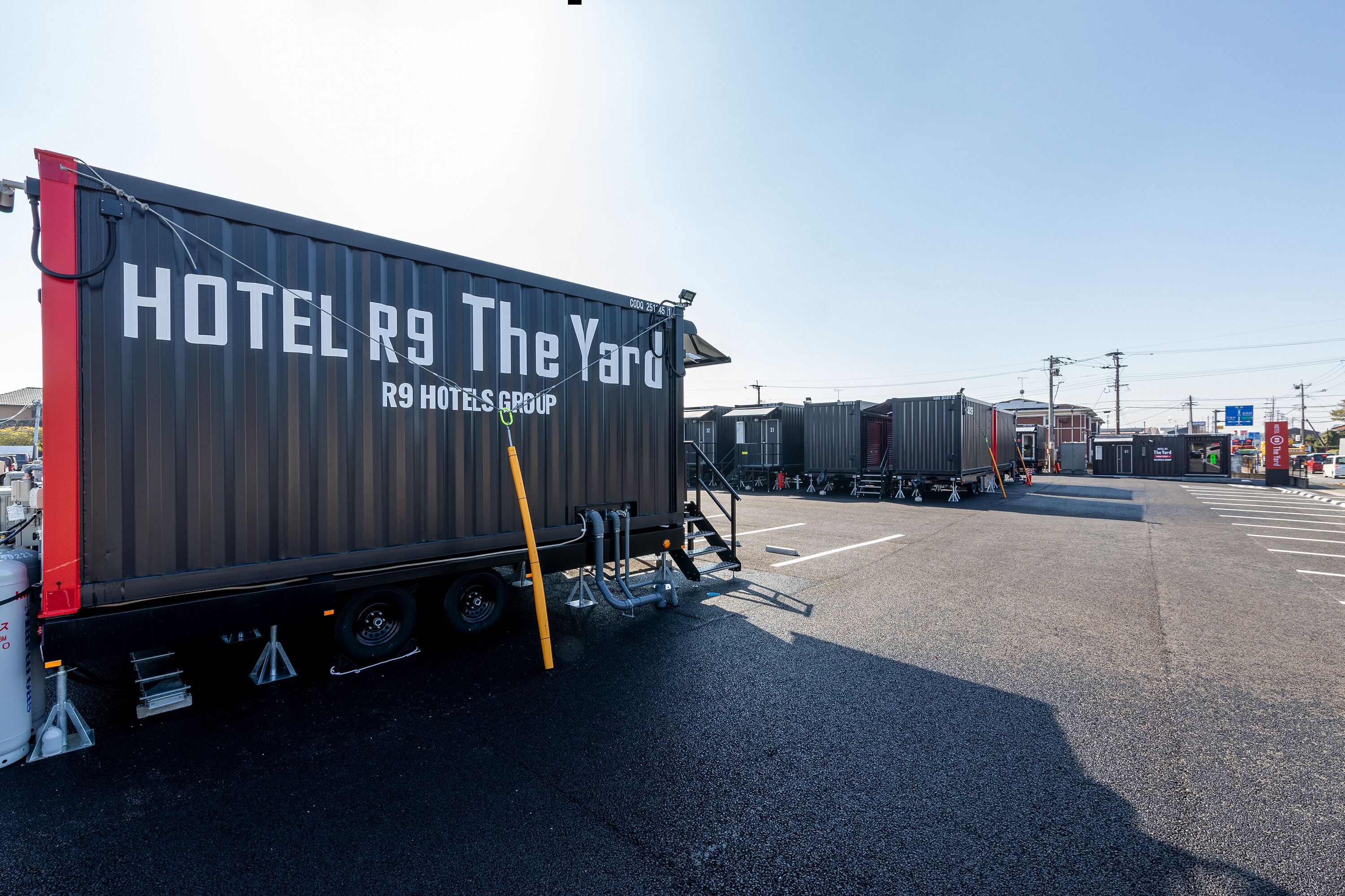 Un camió gran de transport amb la inscripció "HOTEL R9 The Yard" estacionat a un pàrquing.
