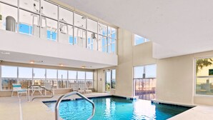 Una piscina interior con agua azul cristalina, una escalera metálica y sillas de descanso junto a la piscina.