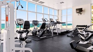 Un gimnasio con máquinas de cardio, equipo de pesas y grandes ventanales con vista al mar.