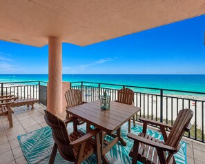 Ein Balkon mit Holztisch und Stühlen, Blick auf den Strand und einem klaren, blauen Himmel.