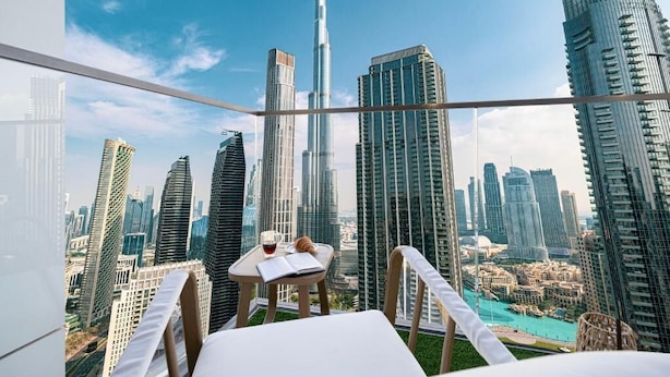 A high-rise room with a city view, a small table with a book and a glass of drink, and a chair. - The Burj Crown Stays by UniDwellers Holiday homes (Dubai)