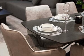Una mesa de comedor dispuesta con platos, cubiertos y una copa de vino, rodeada de sillas acolchadas.
