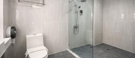 Moderni kylpyhuone, jossa on lasiseinällä varustettu suihku, wc ja käsienkuivaaja.