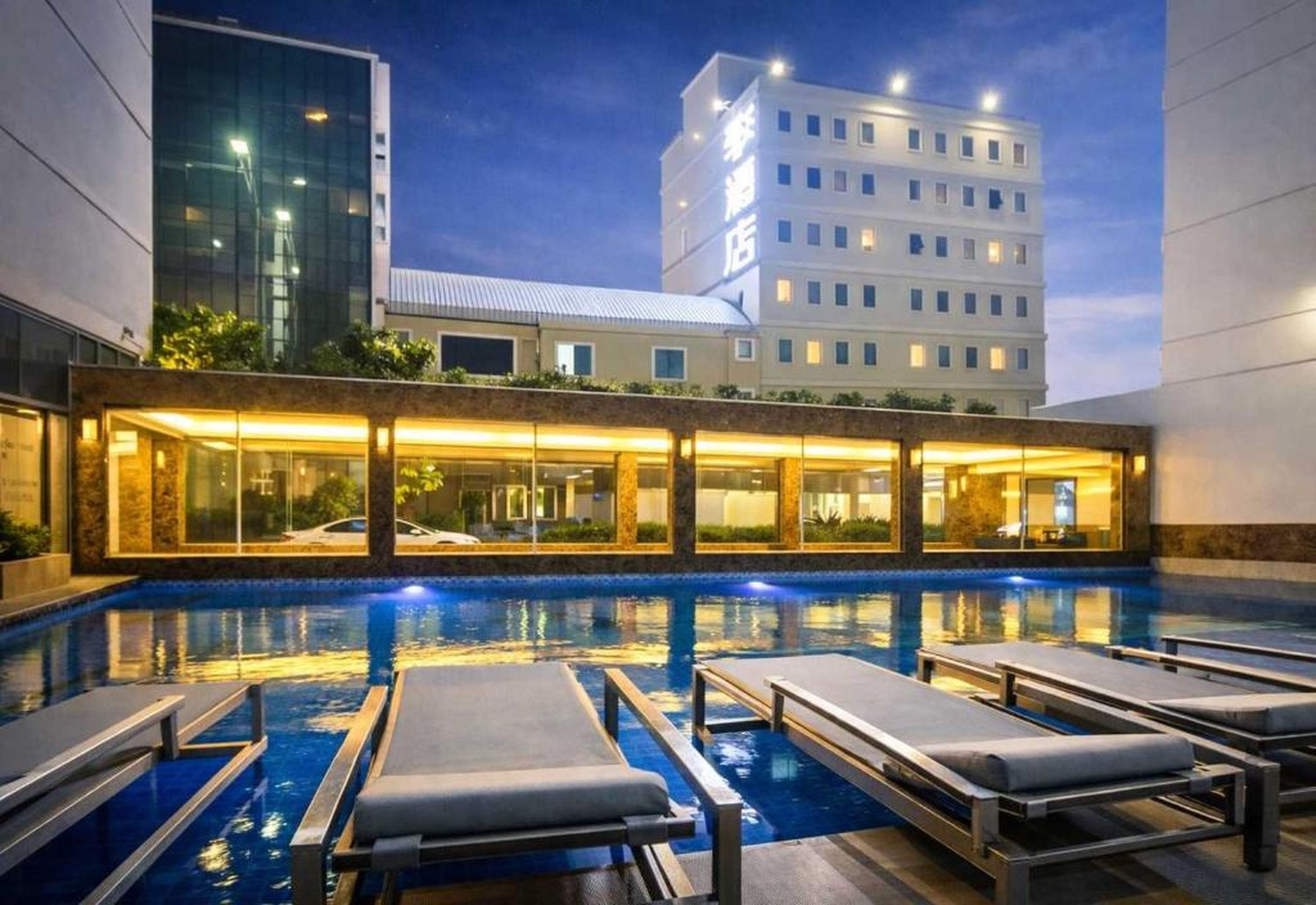 Zona de piscina de hotel con sillones de descanso y un edificio al fondo.