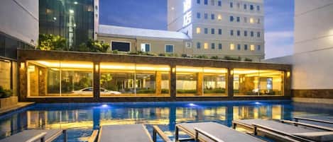 Zona de piscina de hotel con sillones de descanso y un edificio al fondo.