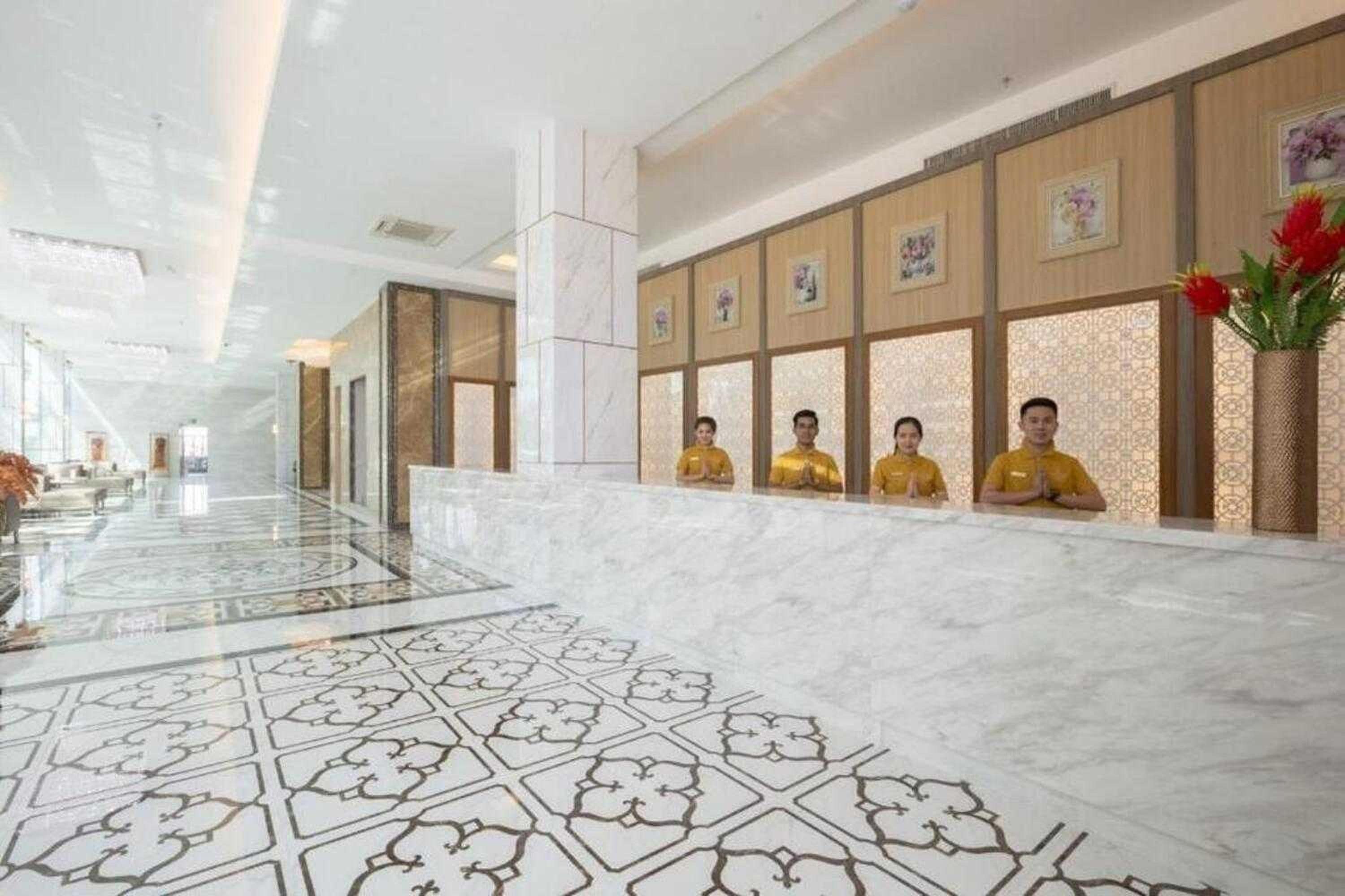 A hotel reception area with a marble floor, a reception desk, and a row of framed pictures on the wall.