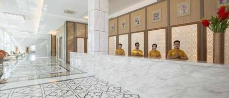 A hotel reception area with a marble floor, a reception desk, and a row of framed pictures on the wall.