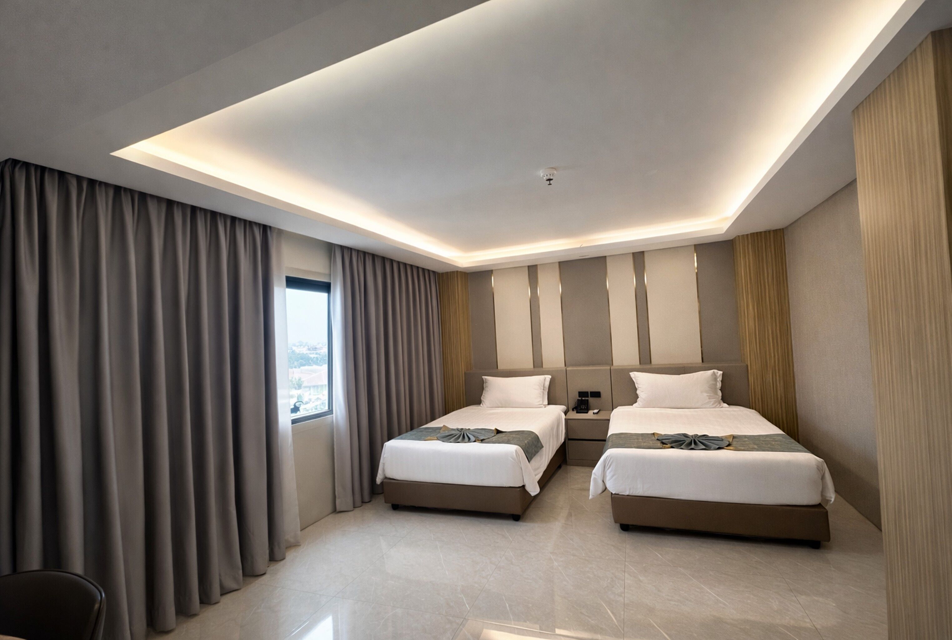 Een moderne hotelkamer met twee bedden, een groot raam en een plafondlamp.