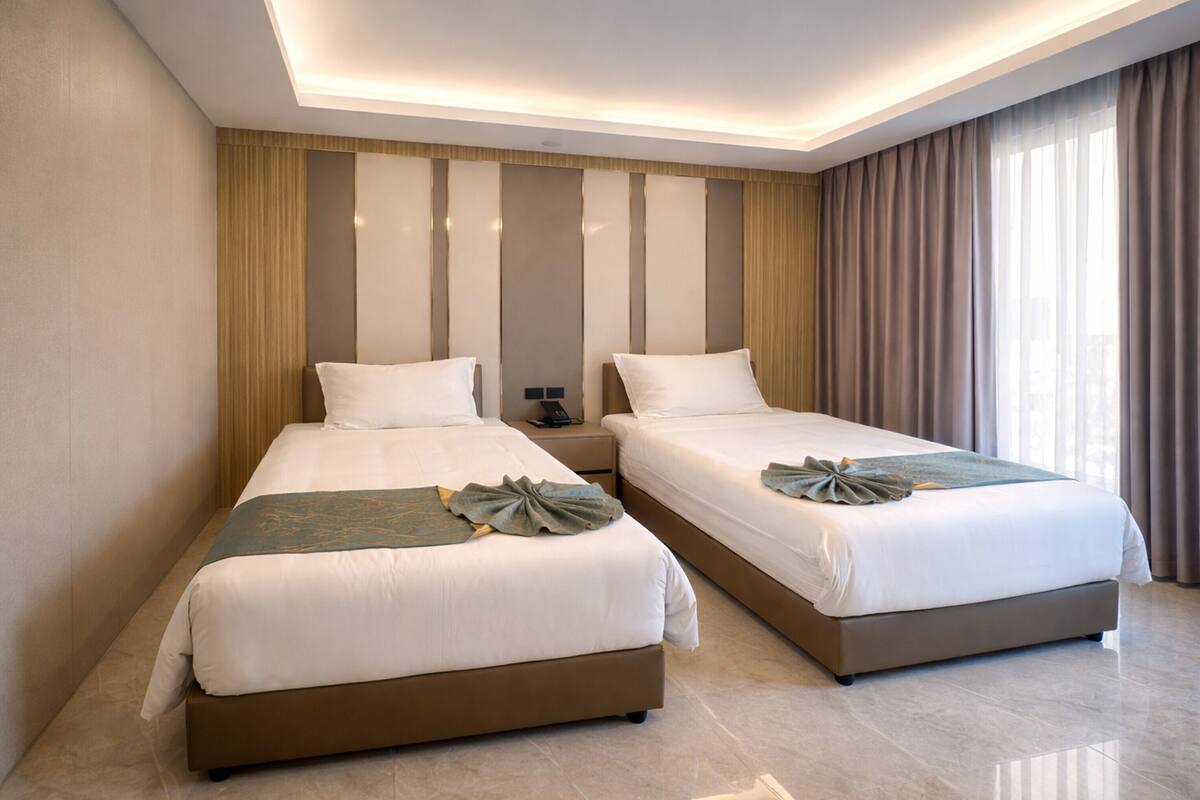 A hotel room with two beds, a nightstand, and a large window with curtains.