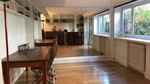 Een ruime kamer met houten vloer, een eettafel met stoelen, een keuken met kastjes en een groot raam dat voor daglicht zorgt.