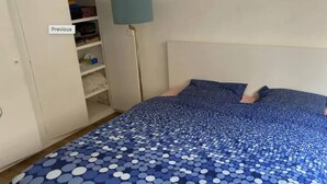 Een slaapkamer met een bed voorzien van een blauwe puntjesdeken, een witte inloopkast en een vloerlamp.