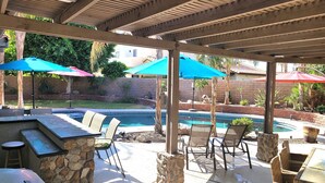 Ein Außenbereich mit Terrasse, Pool, Steinpfeilern und Gartenmöbeln.