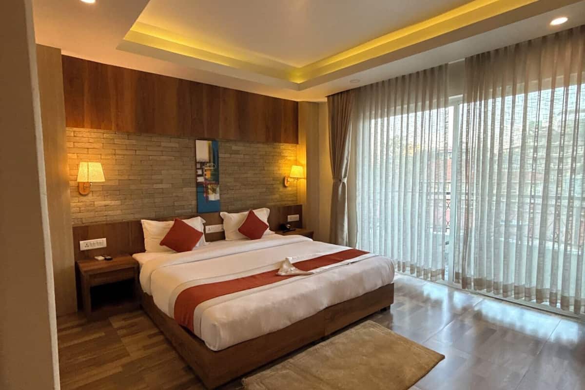 A modern hotel room with a large bed, wooden headboard, two bedside tables with lamps, a stone accent wall, and a large window with curtains.